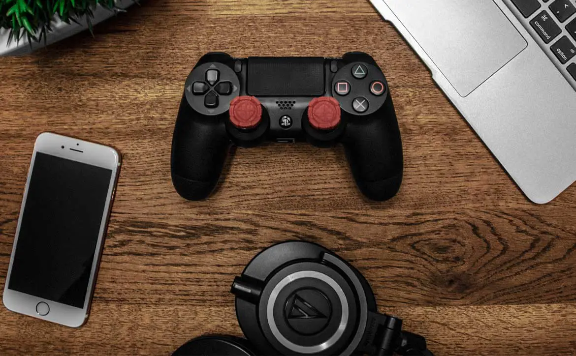 Playstation contoller on desk with iPhone, laptop, and Audio-Technica headphones